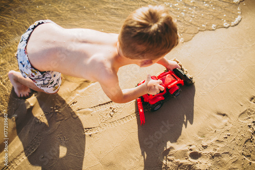 child boy playing on the beach near the river toy red tractor