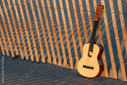 Fotografie six string guitar in sand on beach fence with sunset illumination