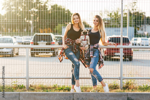 Two beautiful smiling girl sisters twins and dog pug walking in the city