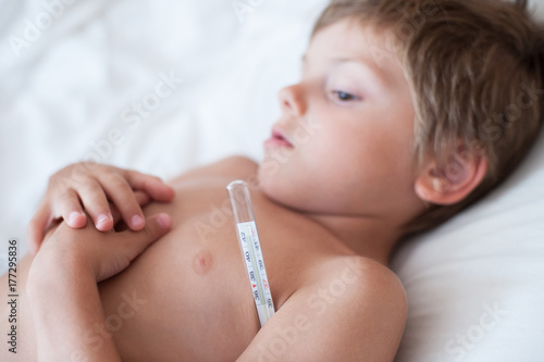 lying caucasian little kid with mercury thermometer underarm