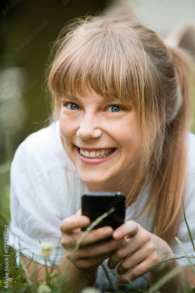 Young woman with fringe lying down on her stomach on grass with mobile phone Young woman with fringe lying down on her stomach on grass with mobile phone