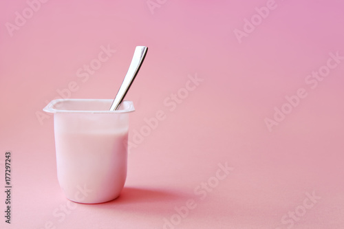 Delicious strawberry yogurt or pudding  in white plastic cup on pink background with copy space. Strawberry pink yoghurt with spoon in it. Minimal style.