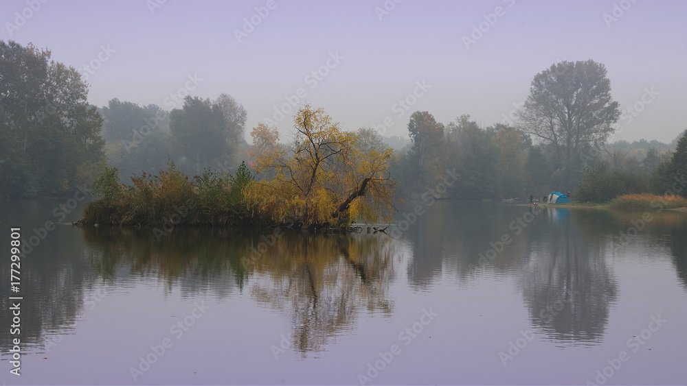 beautiful foggy morning on the lake with the camping fishermen in the distance on the shore, autumn landscape. 16:9 ratio