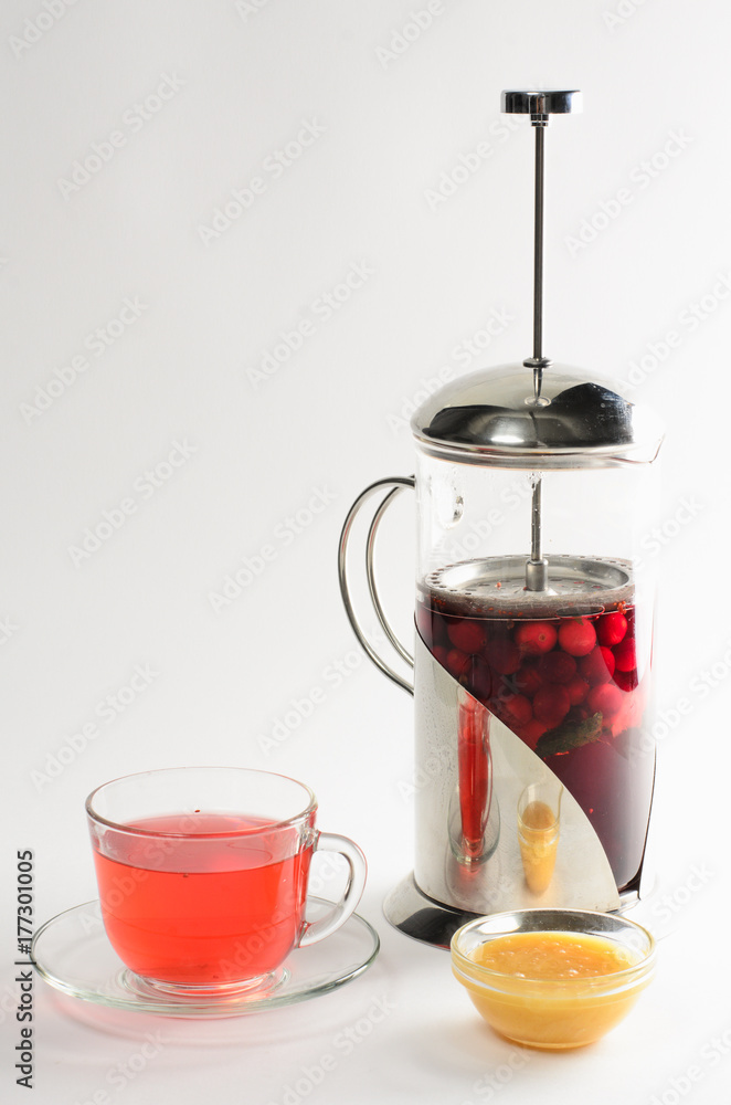 Hot drink of cranberries and raspberries in а teapot and in a cup with honey on white background Hot drink of cranberries and raspberries in а teapot and in a cup with honey on white background