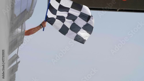 Man holding and waving Checkered race flag in slow motion at finish line on a raceway. Victory, achievement, success and sport concept.