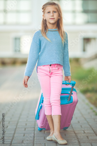 Happy little blonde girl with pink suitcase is ready for travel