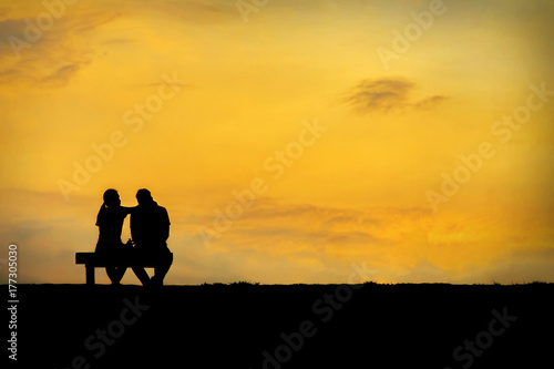 Back view of a couple silhouette sitting on Chair at colorful sunset on background