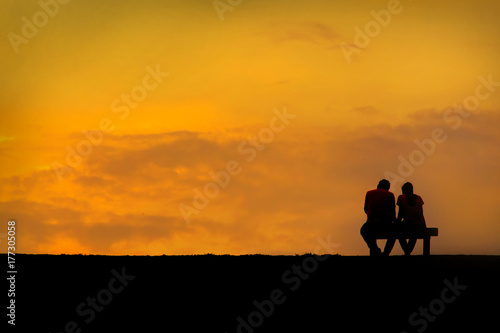 Back view of a couple silhouette sitting on Chair at colorful sunset on background