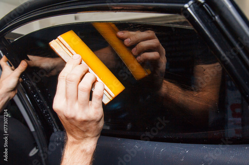 Fotografía Master installs a tint film for the car glass with a hairdryer and spatula with glare of light