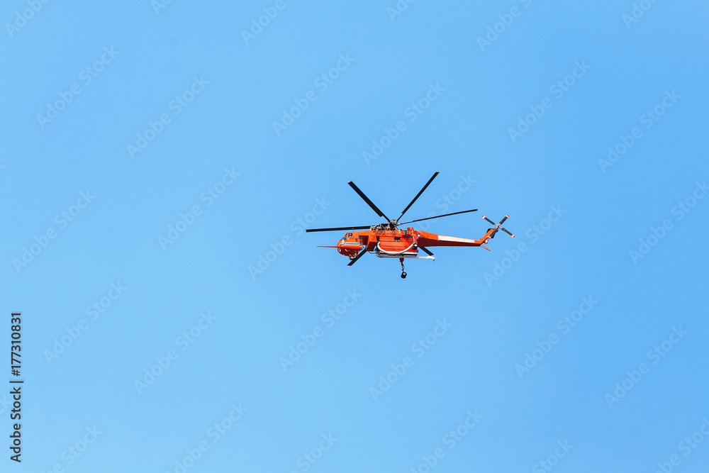 Red firefighter Helicopter flying fast in the blue sky during the emergency call in the city Red firefighter Helicopter flying fast in the blue sky during the emergency call in the city