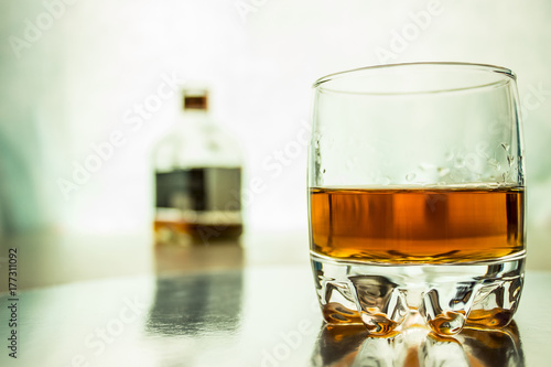 A glass of whiskey with a bottle in the background.