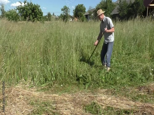 The man is mowing a hight grass with spit.