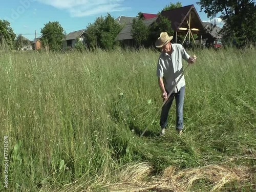 The man is mowing a hight grass with spit.