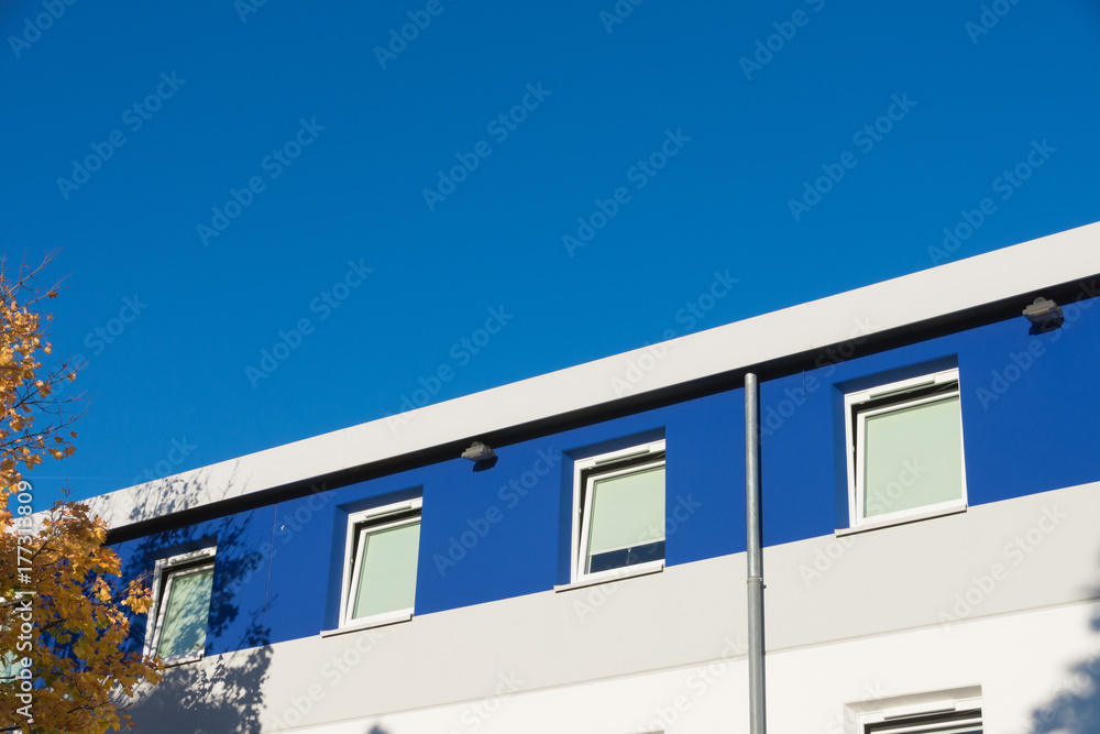 Weiß-blaue Fassade mit Baum im Herbstlaub;