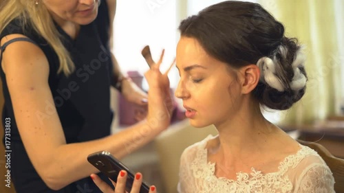 A professional make-up artist does make-up for the bride. The stylist works with the model in preparation for a happy day. The make-up artist works with the skin of the model with tanal cream and photo