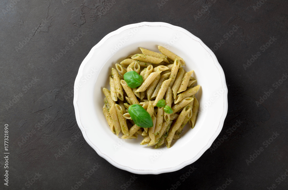 Pasta with homemade pesto sauce in a white plate on a dark stone slate background, top view, copy space