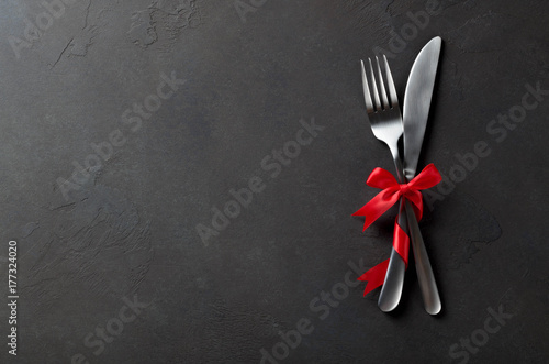 Festive set of cutlery knife and fork with red satin bow, dark stone slate background, top view, copyspace