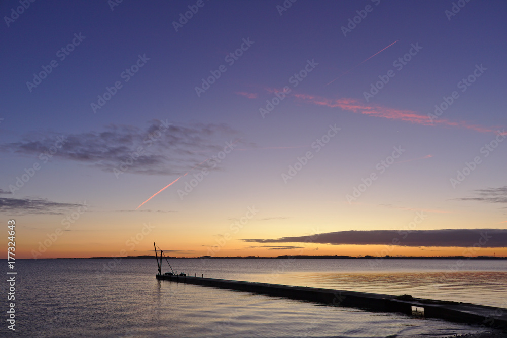 Pier before sunrise with small crane silhouetted against the morning sky and red vapor trail overhead