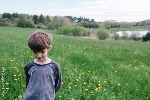 Little boy stands in field with grass in his mouth photo