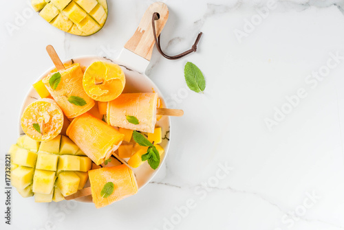 Fototapeta Naklejka Na Ścianę i Meble -  Ice cream, popsicles. Organic dietary foods, desserts. Frozen mango smoothie, with mint leaves and fresh mango fruit, on plate, on white marble table. Copy space top view