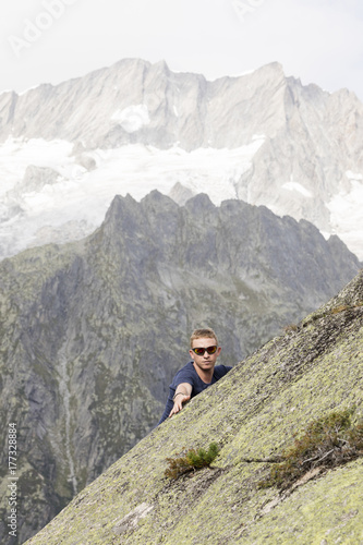 A climber makes climbing exercises on a big rock. In the background, the breathtaking mountain scenery of the Alps
