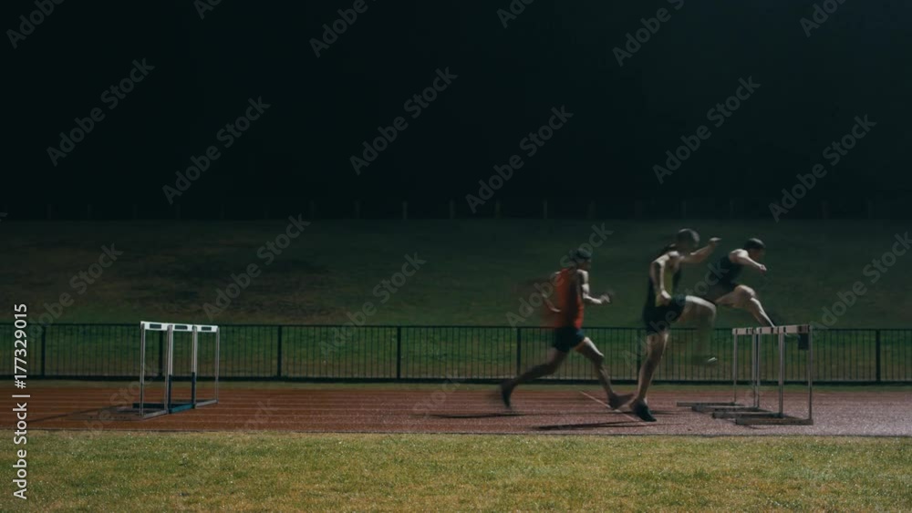 Competitive athletes running & jumping over hurdles at athletics track Competitive athletes running & jumping over hurdles at athletics track