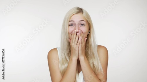 picture of happy woman with long blond hair laughing out loud covering her mouth with hands giggling over white background. Concept of emotions
