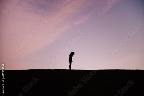 silhouette of a woman in a park looking down at something she dropped photo