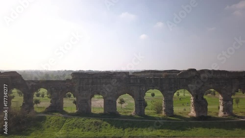 Video from above. Aerial view of the ancient Roman Aqueduct. Old ruins surrounded by a green public Park (Parco degli Acquedotti) Rome, Italy.	 photo