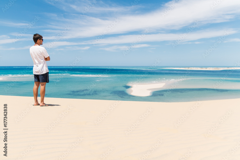 Young man overlooking the ocean from the top of a sand dune on a tropical island Young man overlooking the ocean from the top of a sand dune on a tropical island