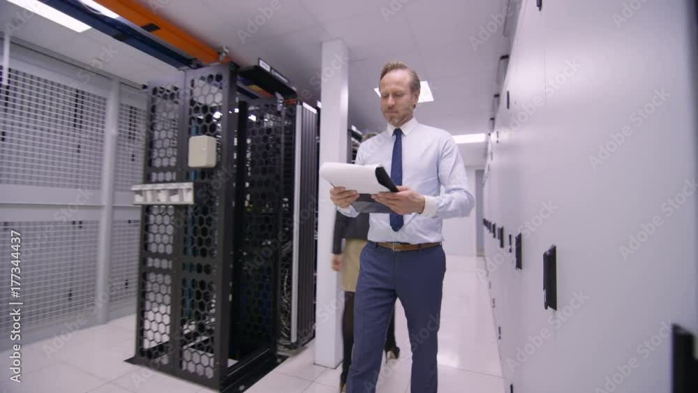 Data administrator walking between rows of server racks and checking the machines. Data administrator walking between rows of server racks and checking the machines.