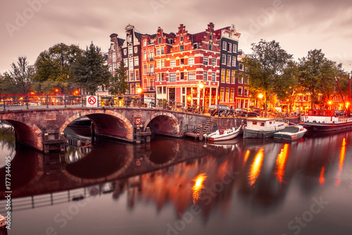 Fototapeta Naklejka Na Ścianę i Meble -  Amsterdam canal, bridge and typical houses, boats and bicycles during evening twilight blue hour, Holland, Netherlands. Used toning