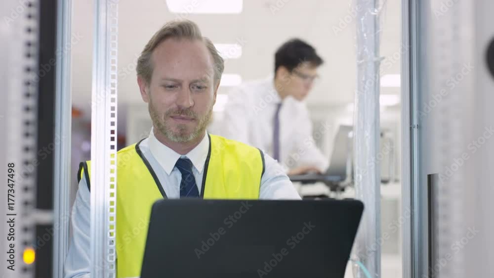 Portrait smiling engineer carrying out checks in a data center server room. Portrait smiling engineer carrying out checks in a data center server room.