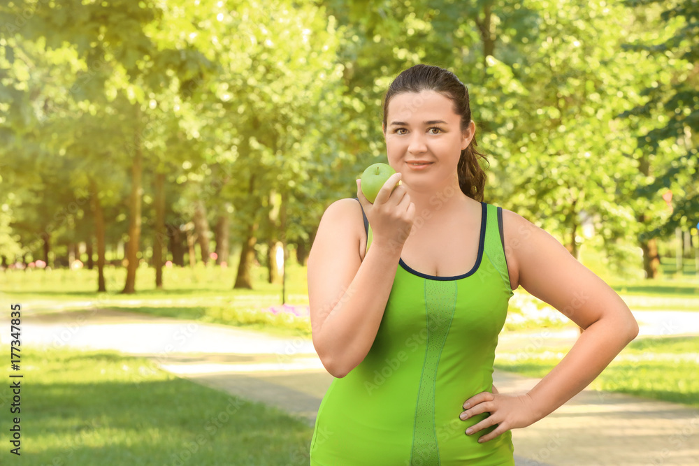 Overweight young woman in sportswear with green apple outdoors. Weight loss concept Overweight young woman in sportswear with green apple outdoors. Weight loss concept
