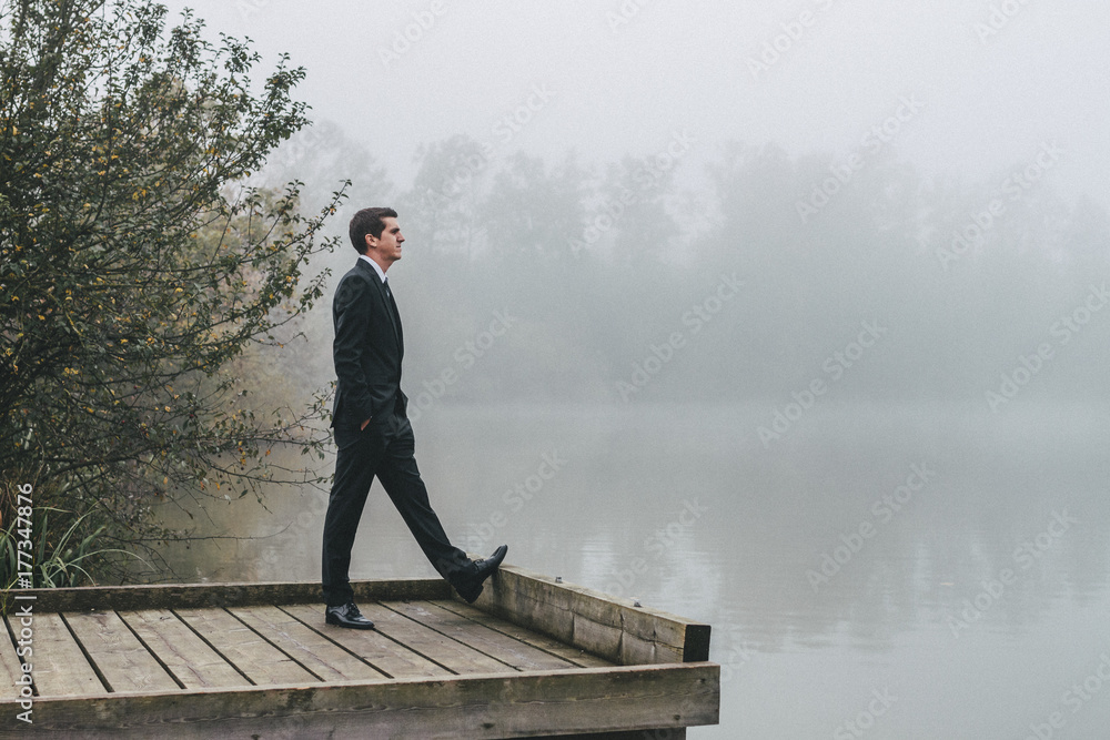 groom standing on a jetty looking at the lake groom standing on a jetty looking at the lake