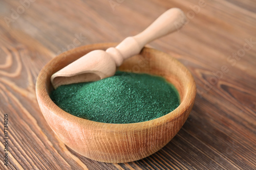 Bowl with spirulina powder and scoop on wooden background