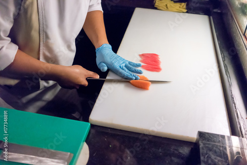 Sushi chef slicing a raw fresh salmon fillet with a sharp knife on a white cutting board