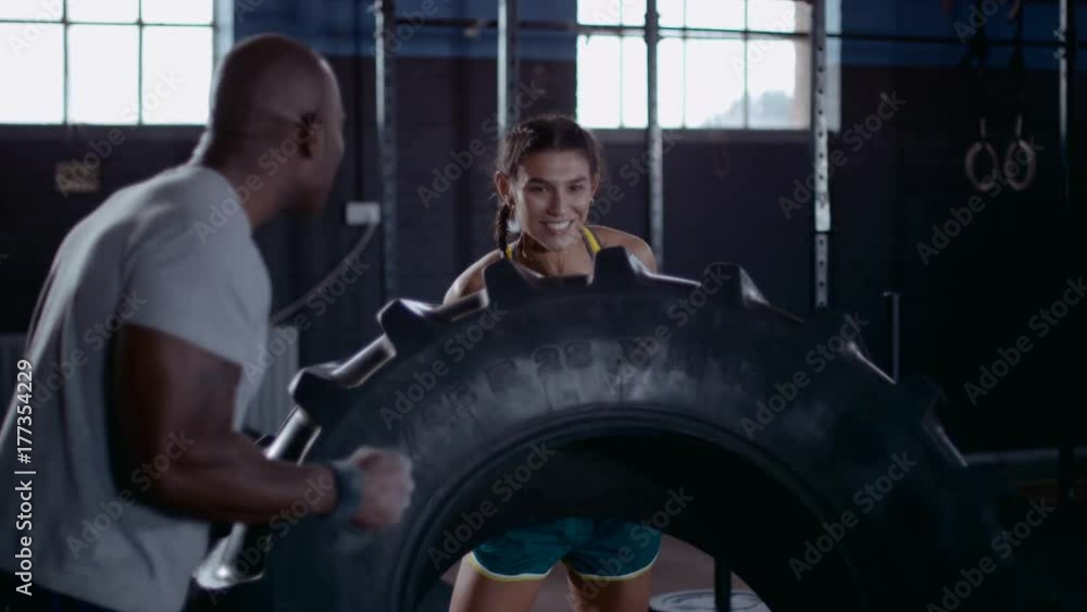 Woman and her fitness instructor cross training with tractor tire at the gym