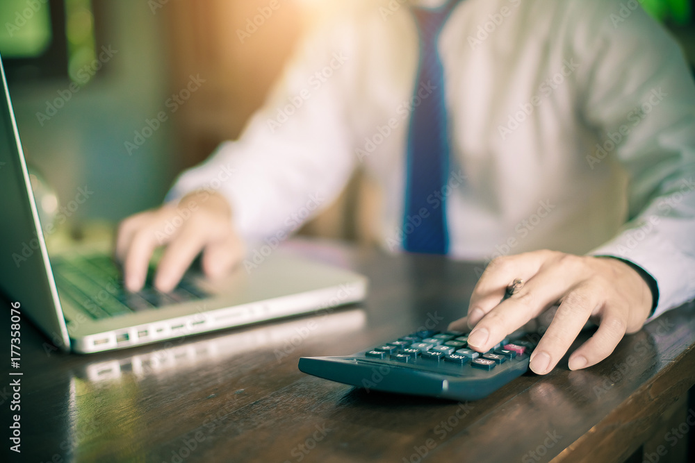Young businessman using a phone and calculator in his office , and economic analysis Young businessman using a phone and calculator in his office , and economic analysis