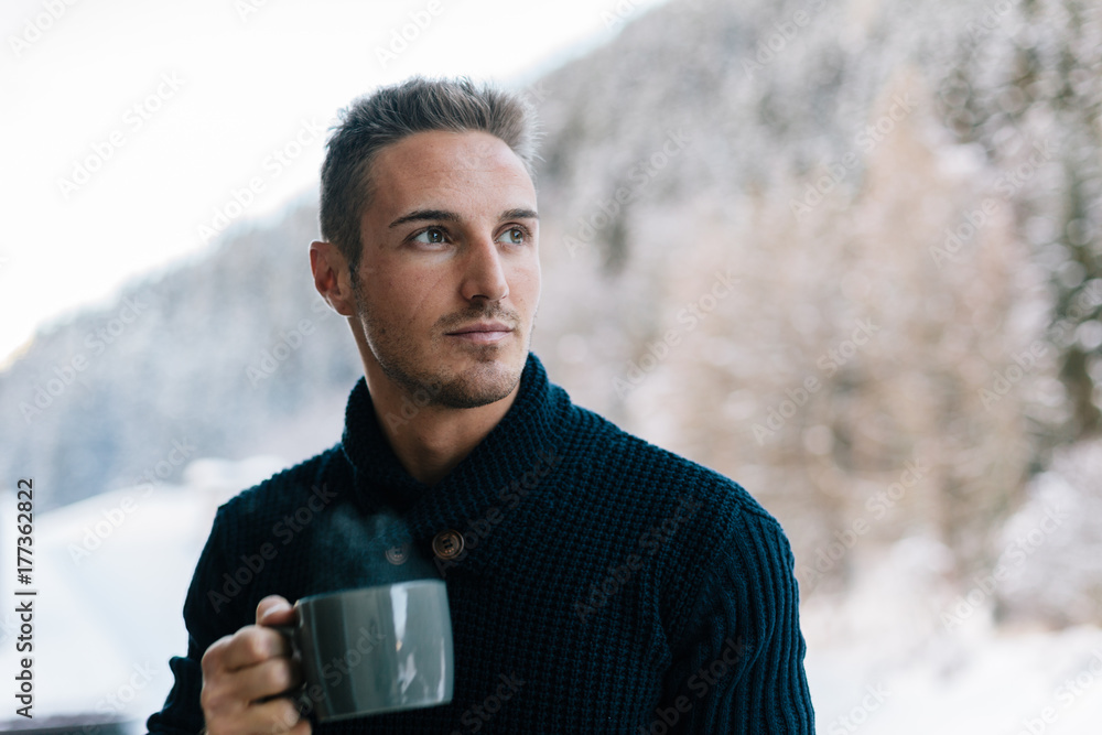 Young man drinking coffee on the balcony in winter Young man drinking coffee on the balcony in winter