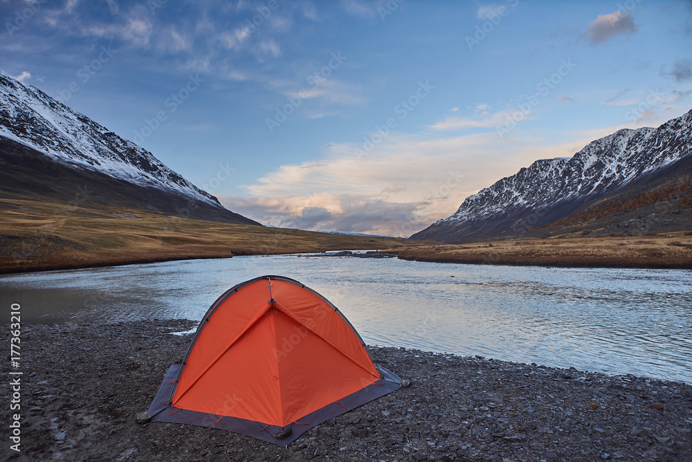 An orange tent near a river in the Mountains