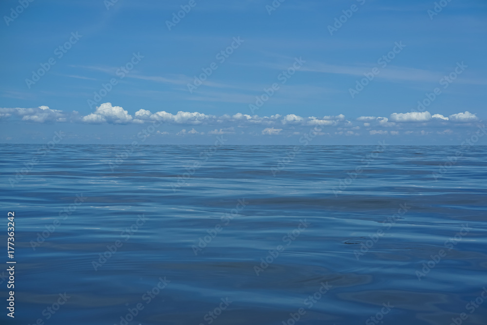 Fototapeta premium Beautiful background scene of gradient blue sky and low raining white cloud above deep blue sea moving water ripple freezing motion with reflection