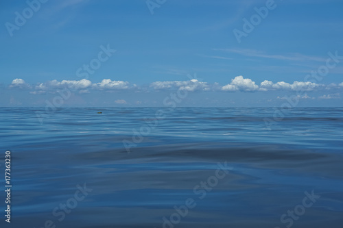 Natural background scene of gradient blue sky horizon and low raining white cloud above deep blue sea moving water ripple freezing motion with reflection
