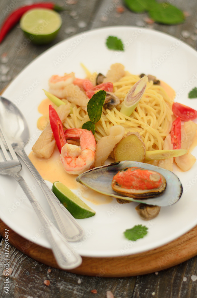 Pasta tom yam with seafood and vegetables on a plate with fork and spoon on wooden background Pasta tom yam with seafood and vegetables on a plate with fork and spoon on wooden background