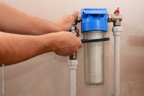 The plumber installs a new cartridge for the water filter. Filter system for water treatment. Installation of a reducer and a water filter for water purification.