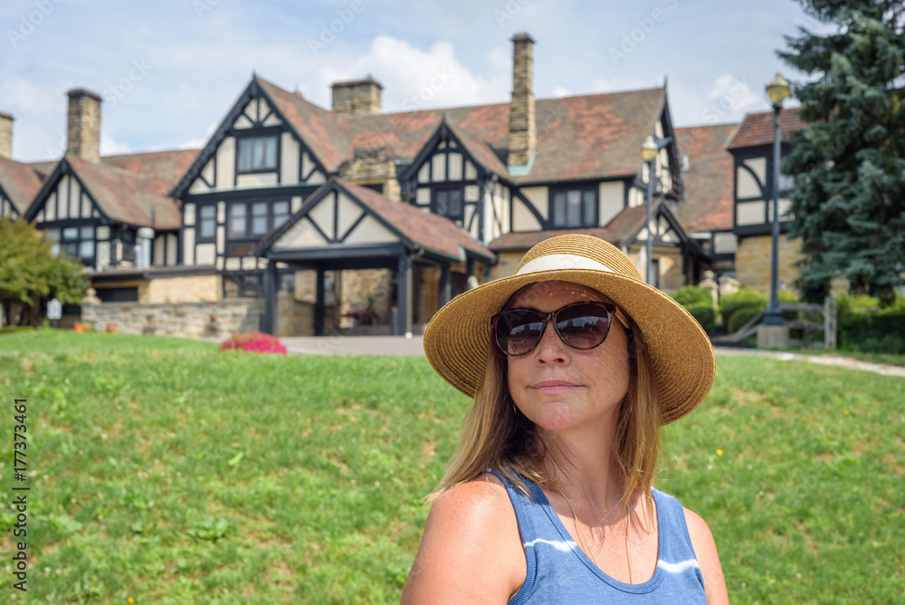 woman in sunhat sitting in front of tudor style mansion
