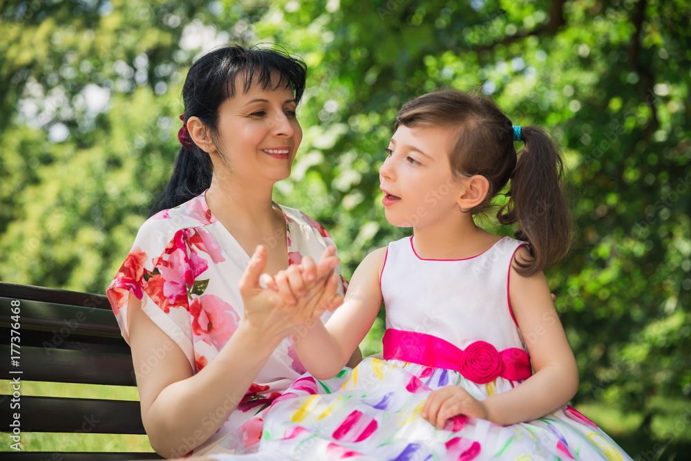 Portrait of young happy mother who sitting on a bench and holding her divine disabled daughter on the laps outdoors Portrait of young happy mother who sitting on a bench and holding her divine disabled daughter on the laps outdoors