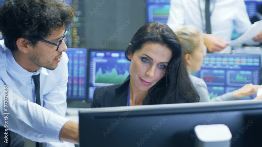 Professional Broker Consults Stock Exchange Trader at Her Workstation. Multi-Ethnic Team at Stock Exchange Office is Busy Selling and Buying Stocks on the Market. Displays Show Relevant Data Numbers. Professional Broker Consults Stock Exchange Trader at Her Workstation. Multi-Ethnic Team at Stock Exchange Office is Busy Selling and Buying Stocks on the Market. Displays Show Relevant Data Numbers.