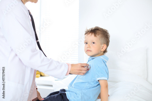 Doctor and patient in hospital. Happy little boy having fun while being examined with stethoscope. Healthcare and insurance concept