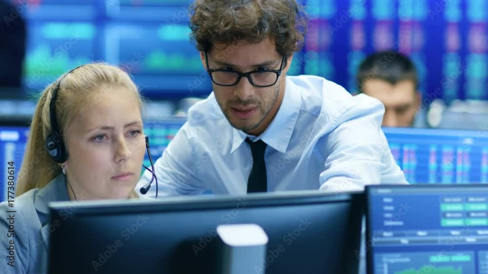 Experienced Stock Exchange Trader Teaches His Apprentice at Her Workstation. Multi-Ethnic Team at Stock Exchange Office is Busy Selling and Buying Stocks on the Market. Experienced Stock Exchange Trader Teaches His Apprentice at Her Workstation. Multi-Ethnic Team at Stock Exchange Office is Busy Selling and Buying Stocks on the Market.